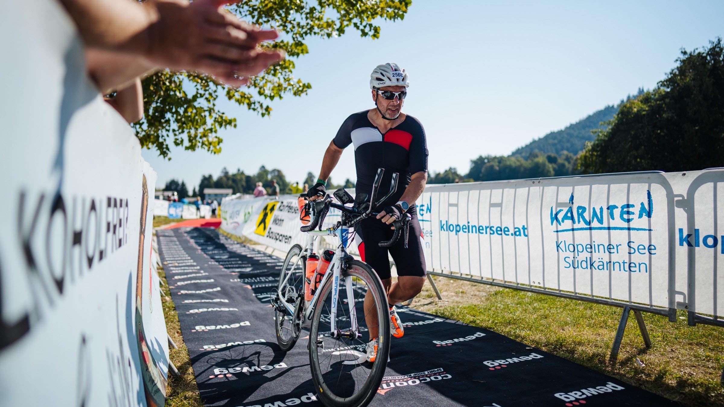 Athlet schiebt sein Rad über den Teppich in die Wechselzone