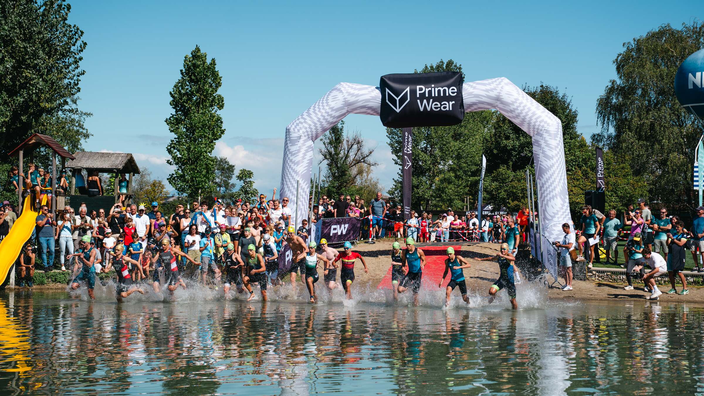 Kinder und Jugendliche laufen beim Start ins Wasser, am Ufer viele Zuschauer