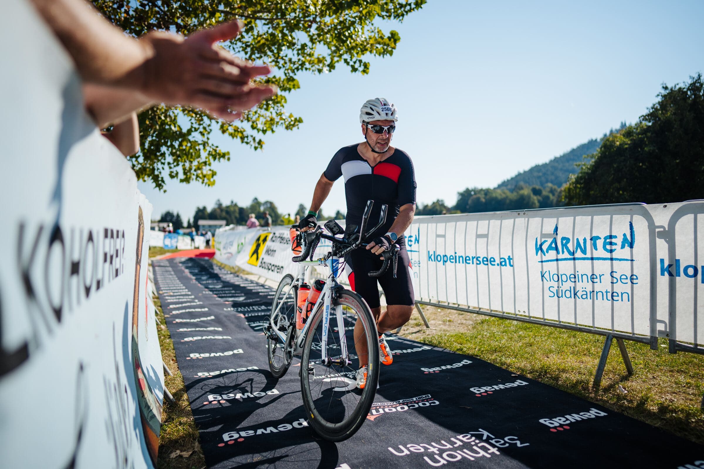 Athlet schiebt sein Rad zwischen den Werbebanden der Partner in die Wechselzone